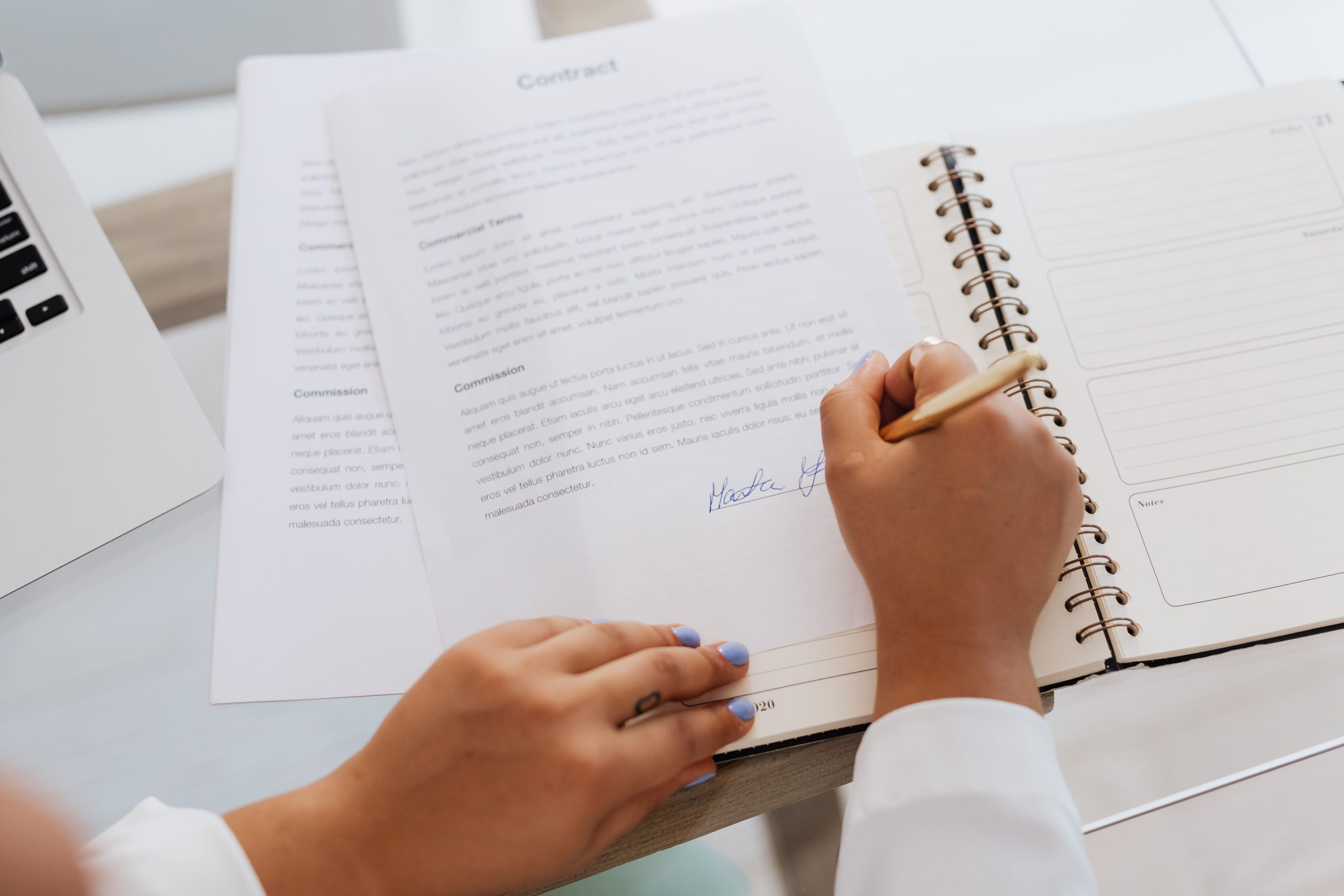 Close-up of hands signing a contract on a desk with office supplies, symbolizing legal agreements