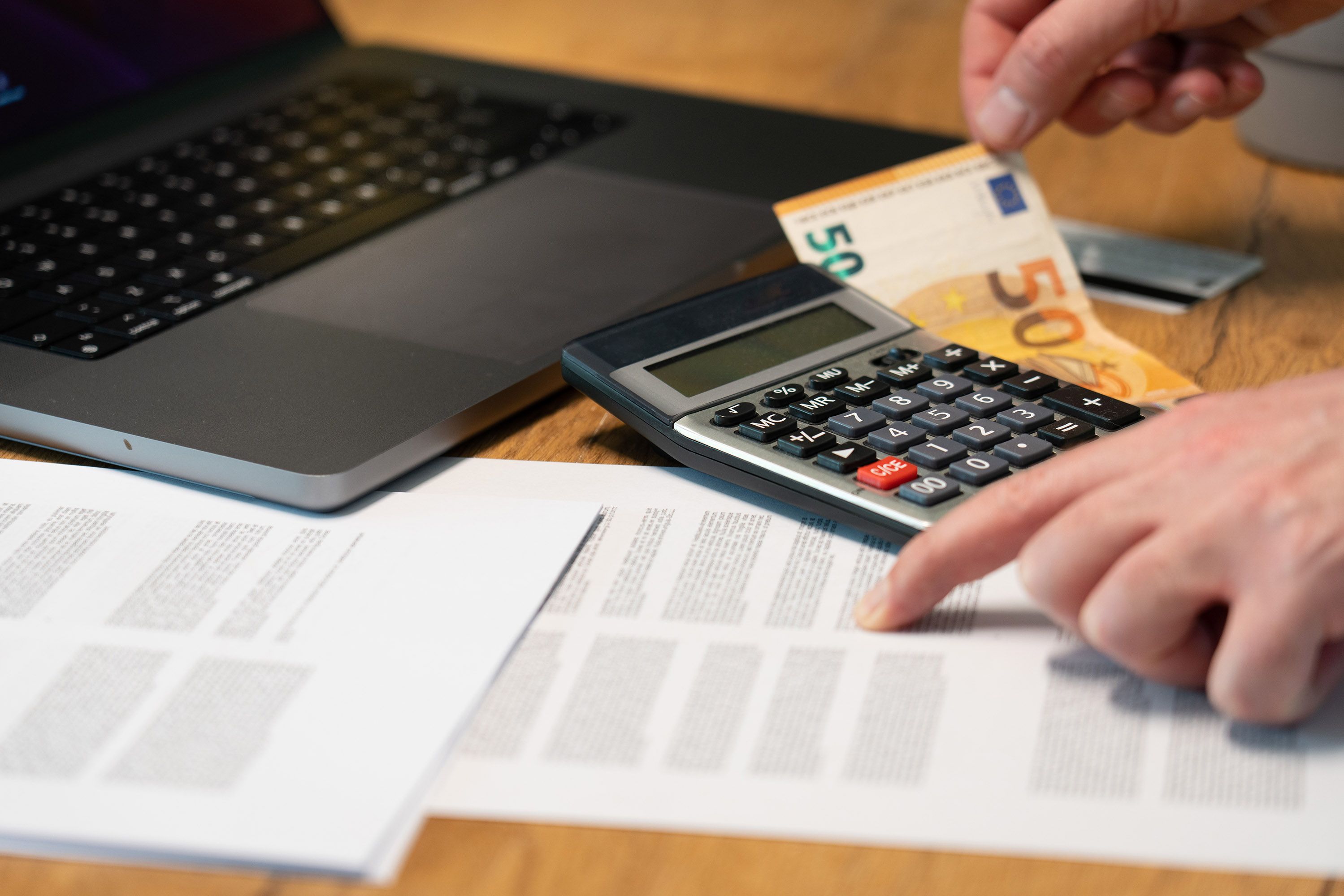 Close-up of hands using a calculator with euro notes and laptop on desk
