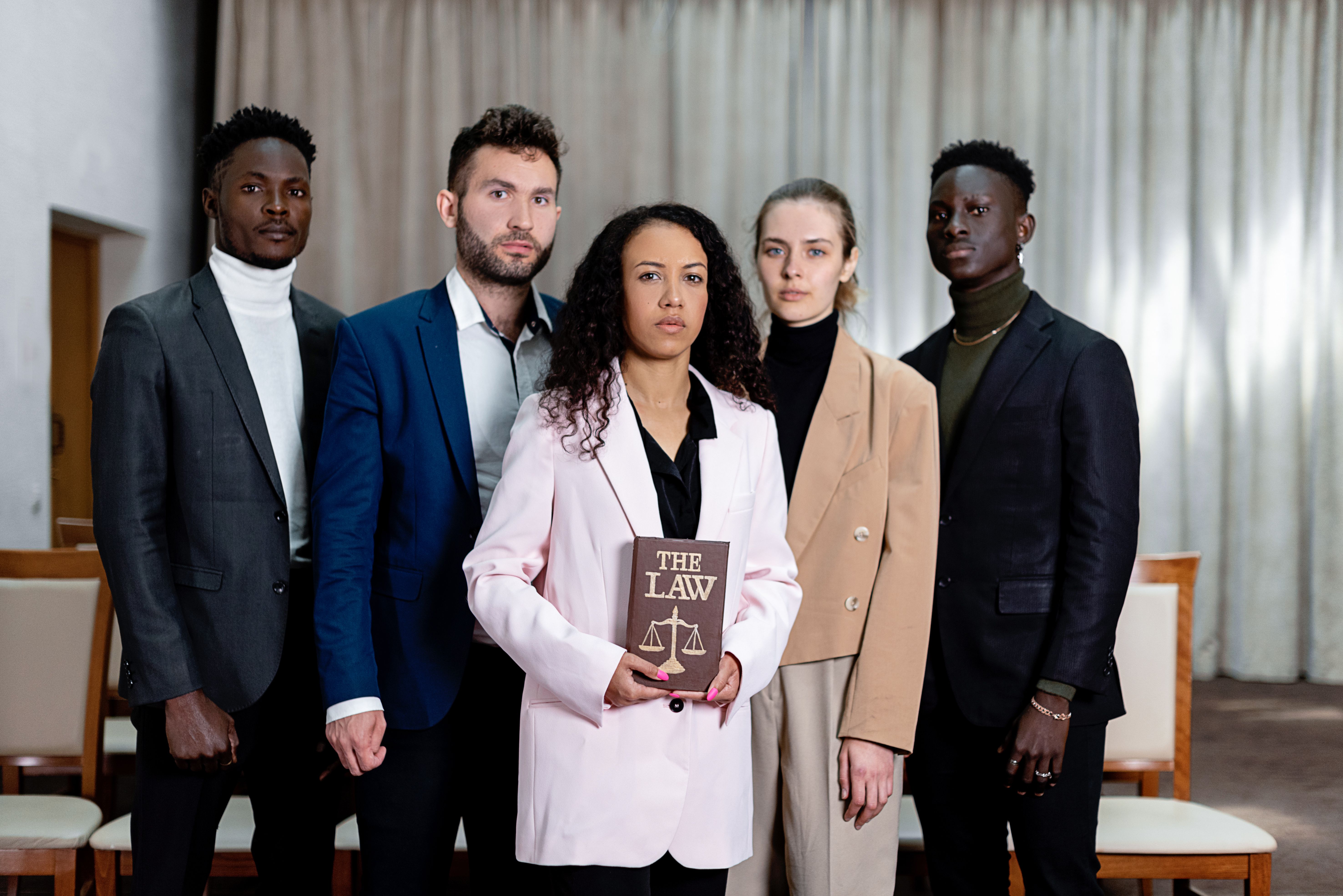 A diverse group of five lawyers posing confidently with a law book in an office setting
